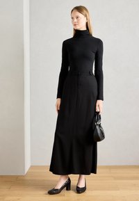 Black turtleneck top paired with a long black skirt, featuring a smooth texture. Black handbag and patterned heels complete the outfit.