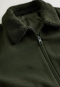 Dark green fleece jacket with a fuzzy collar and a partially zipped silver zipper on a plain light background.
