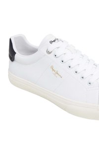 Sneaker bianche realizzate in materiale sintetico liscio, con un accentuazione nera sul tallone e dettagli del logo dorato. Design classico con lacci.