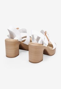 Sandalias de tacón blanco con diseño de tiras cruzadas, tacones de bloque de madera y una amplia correa para el tobillo con un acento de hebilla metálica.