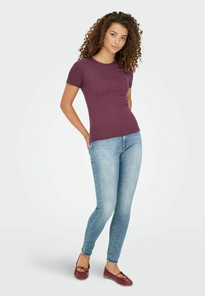 Burgunderfarbens, strukturiertes Kurzarmoberteil, kombiniert mit hellblauen, enganliegenden Jeans und maronenfarbigen Ballerinas mit einer Schleifendetail.