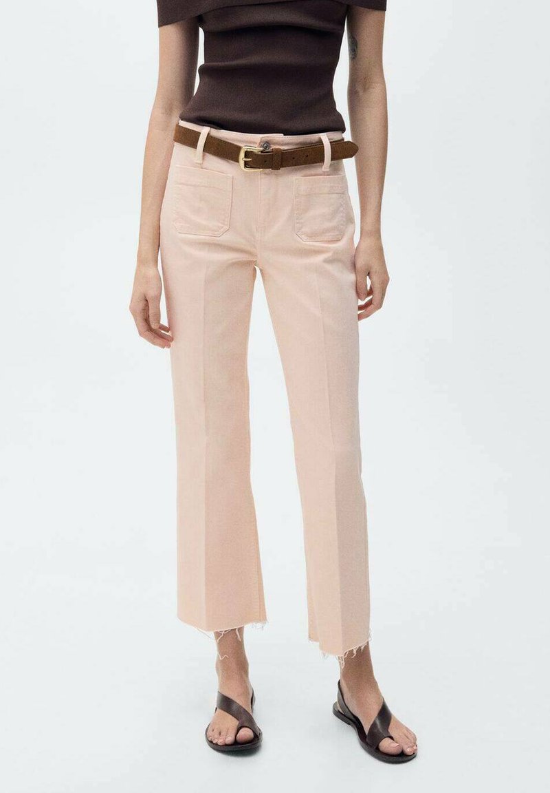 Jean cropped rose clair avec ourlets effilochés, deux poches arrière et une ceinture marron. Associé à un haut marron ajusté et des sandales noires.
