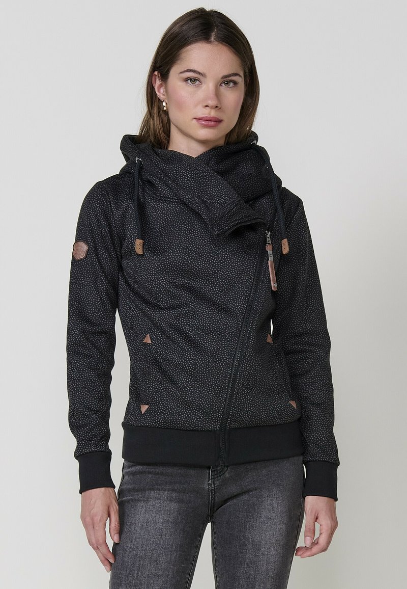 Felpa nera con zip e colletto alto, tessuto testurizzato, dettagli triangolari e particolari simili alla pelle. Presenta un cordino regolabile.