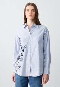 Camicia button-up a righe blu chiaro con maniche lunghe, caratterizzata da una stampa floreale scura sul lato sinistro e una tasca sul petto per un tocco di dettaglio.