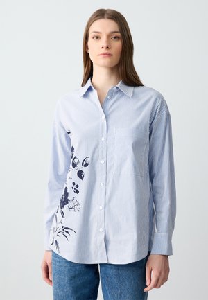 Camicia button-up a righe blu chiaro con maniche lunghe, caratterizzata da una stampa floreale scura sul lato sinistro e una tasca sul petto per un tocco di dettaglio.