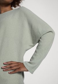 Ljusgrön, ribbad tygtop med lös passform och överdimensionerade ärmar. Texturerad yta, rundad halsringning och sydda fålldetaljer.