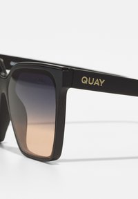 Black sunglasses with a rectangular frame, gradient lenses transitioning from dark to light, featuring gold "QUAY" branding on the arm.