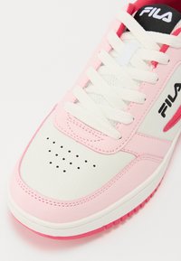 Zapatilla blanca y rosa con material texturizado, puntera perforada, cordones blancos y acentos rojos. Presenta el logo de Fila en el lateral.