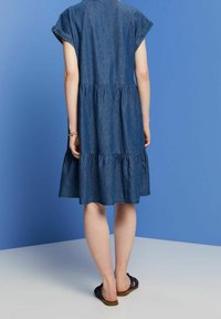 Denim dress featuring short sleeves, a tiered hem, and a relaxed fit, displayed against a solid blue background.