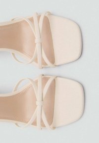 Beige Absatzsandalen mit quadratischer Zehenform, die dünne überkreuzte Riemen und eine glatte matte Oberfläche aufweisen. Die Innensohle ist leicht gepolstert.
