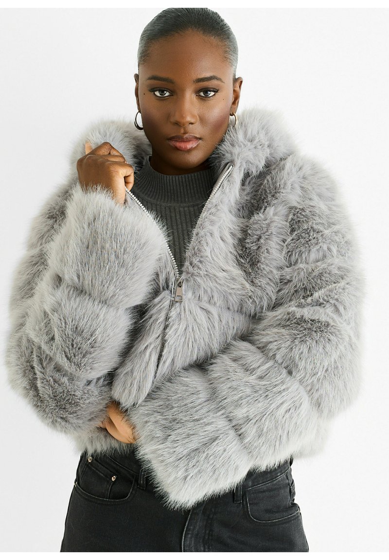 Gray faux fur jacket with a hood, zip closure, puffy sleeves, and textured detailing. Worn over a ribbed gray top and black pants.