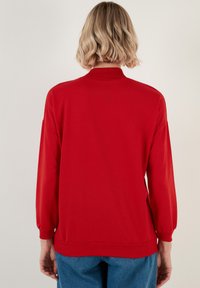 Sudadera roja de manga larga con cuello alto y puños acanalados. Presenta un color sólido, textura suave y un corte relajado.