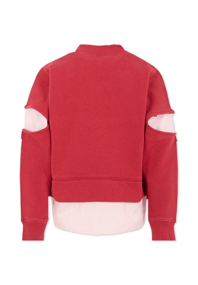 Felpa corta rossa con maniche lunghe e dettagli tagliati, sovrapposta a un tessuto a coste rosa chiaro all'orlo inferiore.