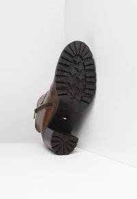 Bruine leren enkelboot met een zijrits, voorzien van een gestructureerde rubberen zool met multidirectionele groeven en een opvallend logo.