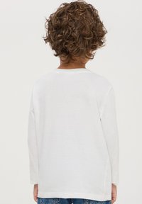 T-shirt bianco a maniche lunghe in morbido cotone, con vestibilità comoda e scollatura tonda, indossato con jeans blu.