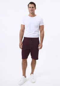 Hvid crew neck t-shirt, parret med maroon mønstrede shorts med justerbar talje. Modellen bærer hvide sneakers.