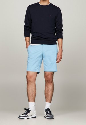 Marineblauer Pullover mit Rundhalsausschnitt, hellblaue Shorts und schwarz-weiße Sneaker. Gerundeter Ausschnitt, strukturierter Pullover und mehrfarbiges Sneaker-Design.