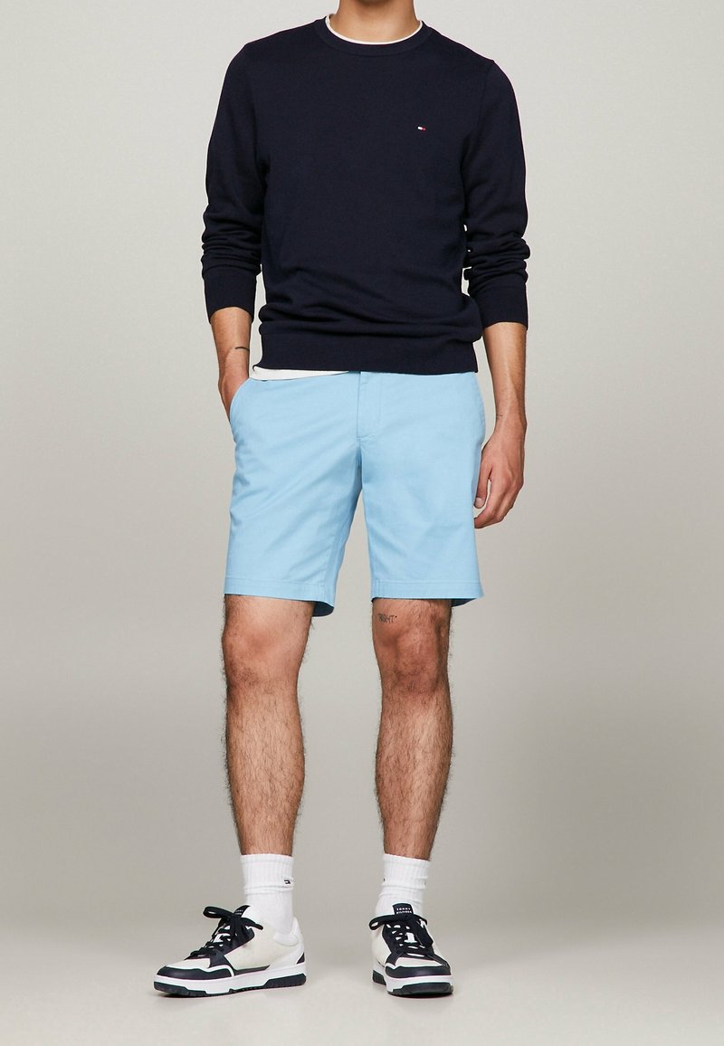 Pull ras du cou bleu marine, short bleu clair et baskets bicolores noir et blanc. Encolure arrondie, pull texturé et design multicolore des baskets.