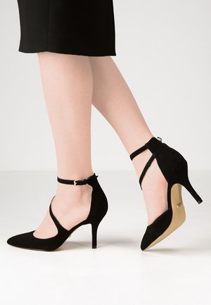 Černé semišové boty na vysokém podpatku s špičatými špičkami, kotníkovými pásky a stiletto podpatkem o výšce 3-4 palce. Hladká textura a štíhlý design.