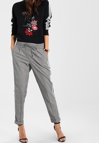 Sweat-shirt noir avec broderie florale, manches rayées grises ; pantalon de jogging à carreaux gris avec cordon de serrage et ourlets retroussés, associé à des talons noirs.