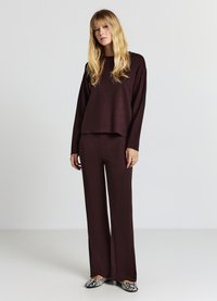 Bordeauxroter Strickpullover mit langen Ärmeln, kombiniert mit passenden weiten Hosen. Glatte Textur, lockere Passform, ergänzt durch gemusterte Ballerinas.