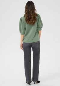 Roheline puff-sleeve top vabamoe ja tumedate hallide sirgete pükstega. Sile tekstuur, lõdva disain ja nähtavaid mustreid pole.