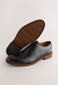 Schwarzer Lederschuh mit glatter Oberfläche, Kappenzehen-Design und brauner Gummisohle. Verfügt über einen klassischen Schnürstil und tonale Nähte.