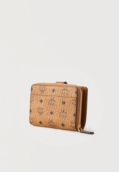 Portefeuille compact en cuir marron clair avec logo MCM noir et motifs en losange, compartiment zippé et poche avant plate sur fond uni.