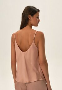 Jasnoróżowy satynowy top na ramiączkach z niskim dekoltem z tyłu, cienkimi regulowanymi ramiączkami i gładką fakturą. Prosty krój bez wzorów i ozdób.