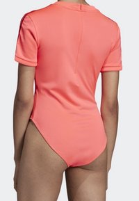 Jednodílné plavky s krátkým rukávem, těsně přiléhající, v jasně korálové barvě, vyrobené z hladkého, elastického materiálu a s nízkým výstřihem na zádech a diskrétním zipem.