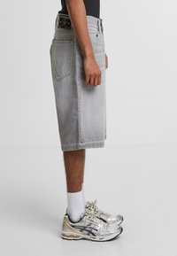 Szare dżinsowe szorty o luźnym kroju, z postrzępionym dołem i dwiema tylnymi kieszeniami. Noszone z białymi skarpetkami i metalicznymi butami do biegania.