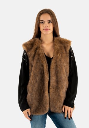 Gilet in pelliccia sintetica marrone con apertura frontale, caratterizzato da una finitura texturizzata. Maniche nere in contrasto decorate con paillettes. Indossato con una maglietta nera e jeans blu.