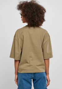 Khaki oversize bavlněné tričko s krátkými rukávy, kulatým výstřihem a volným střihem. Měkká textura s minimálními švy na dolním okraji.