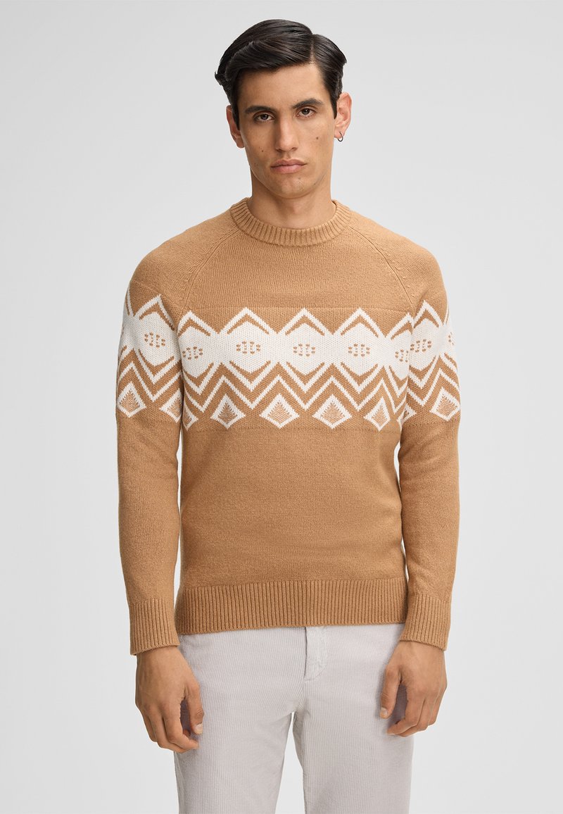 Beżowy sweter z dzianiny z białym geometrycznym wzorem na klatce piersiowej, okrągłym dekoltem oraz ściągaczami przy mankietach i dolnej k rawędzi.