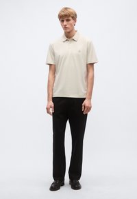 Béžové polokošeľa s golierom a malým logom, kombinovaná s čiernymi nohavicami a mokasínami. Hladká bavlnená textúra, voľný strih.