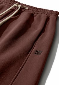 Burgundijas krāsas sporta bikses no mīksta auduma ar elastīgu jostu, ar krēms krāsas mežģīti un nelielu melnu logotipu blakus kabatai.