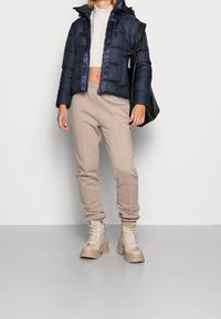 Marinblå puffjacka med huva, beiga sweatpants och beiga klumpiga stövlar. Slät textur med quiltat mönster. Svart axelväska.