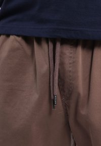 Shorts en tissu marron avec une taille élastique et un cordon de serrage assorti. Matière en coton texturée avec des détails de couture visibles.