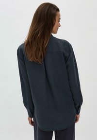 Camicia a maniche lunghe blu navy con polsini abbottonati e orlo curvo, realizzata in tessuto morbido, con yoke posteriore e dettagli in plissettatura.