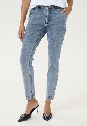 Jeans en denim bleu clair avec une jambe fuselée, un léger délavage et un design classique à cinq poches. Portés avec des talons aiguilles noirs.