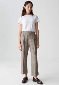 Grijze geruite broek met een hoge taille en wijde pijpen, voorzien van opgerolde boorden. Gecombineerd met een plain wit t-shirt en donkere instappers.