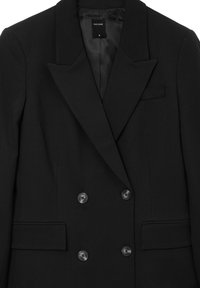 Blazer noir à double boutonnage avec un col à revers, tissu texturé, deux poches à rabat sur le devant et fermetures à boutons noirs. Étiquette de marque visible.