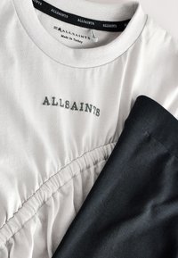 Bijela majica s naboranim uzorkom i sivošivom izvezenim natpisom "ALLSAINTS"; crni donji dio od glatkog tkanja; obilježen unutarnjom oznakom brenda na ovratniku.