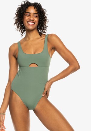 Maillot de bain une pièce côtelé vert kaki avec un décolleté carré et un détail découpé à la taille ; il dispose de bretelles larges et d'une couverture moyenne.
