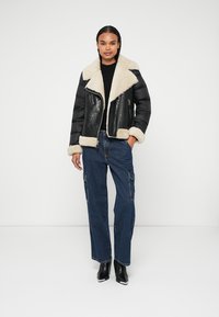 Schwarze Kunstlederjacke mit Schafsfellkragen und -manschetten, kombiniert mit lässigen blauen Cargo-Jeans und schwarzen Ankle Boots.