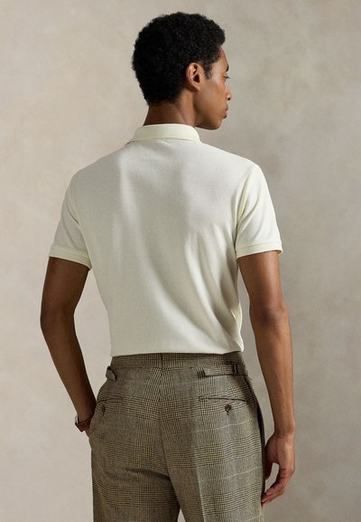 Μπεζ κοντομάνικο πόλο με υφή στην επιφάνεια, συνδυασμένο με καφέ καρό παντελόνι με διακριτικό μοτίβο και πίσω τσέπες.