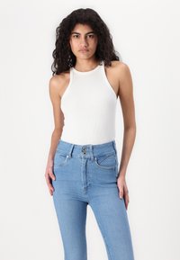 Hvit ribbet tanktop kombinert med høytlivs lyseblå denimbukser med knappelukking og to frontlommer.