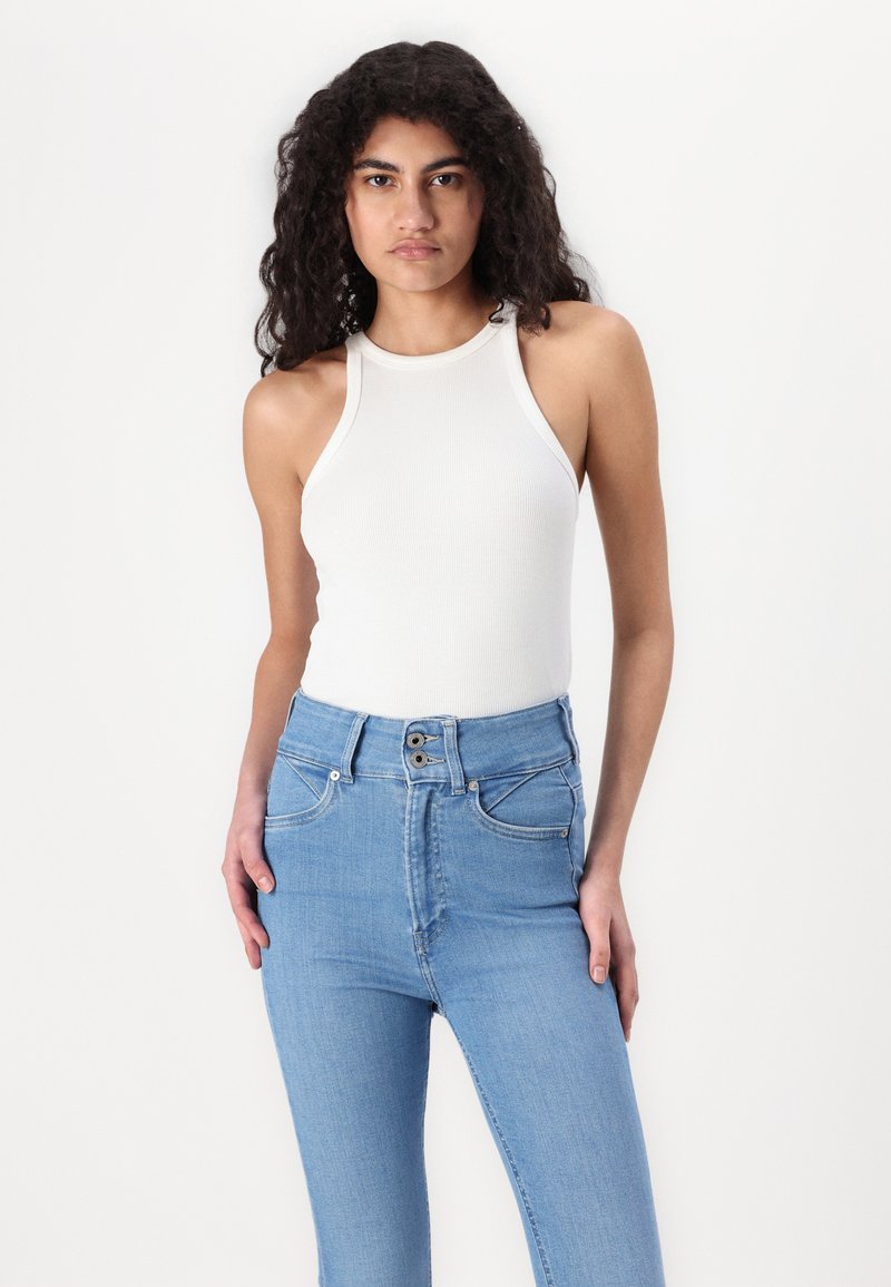 Weißes, geripptes Tanktop kombiniert mit hoch taillierten hellblauen Jeans aus Denim, die einen Knopfverschluss und zwei Fronttaschen haben.