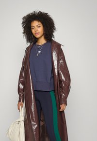 Blank vinröd vinyl överrock, mörkblå sweatshirt och marinblå leggings med gröna sidosstreck. Accessoar: krämfärgad handväska med tvinnad detalj.