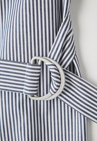 Marineblå og hvitstripet stoff med en metall D-ring spenne, med en sidelås med "TOMMY HILFIGER" gravert. Glatt tekstur og skreddersydd design.